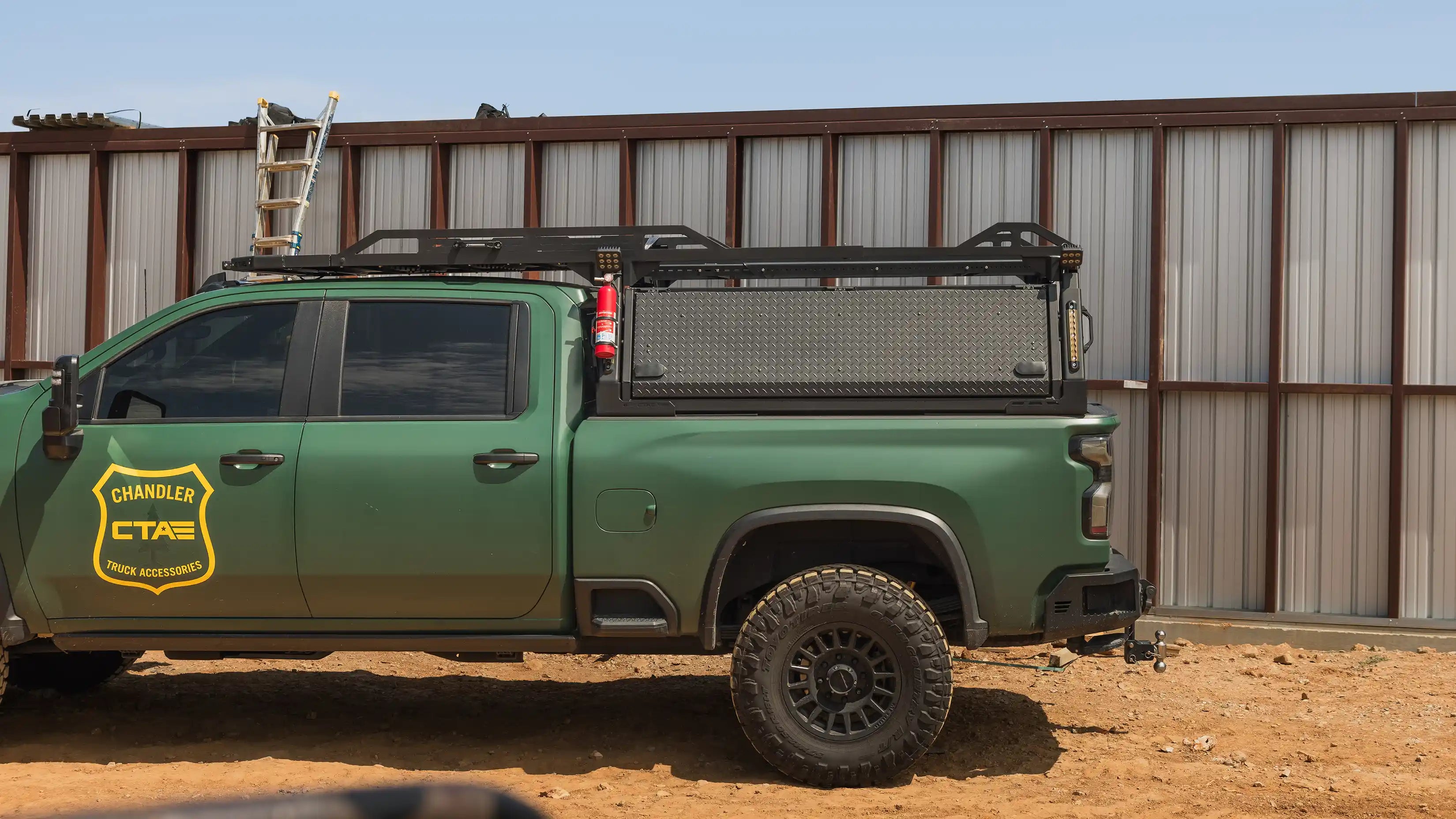 Green pickup truck with truck bed storage system including a ladder rack and side mounted tool boxes on a construction site.